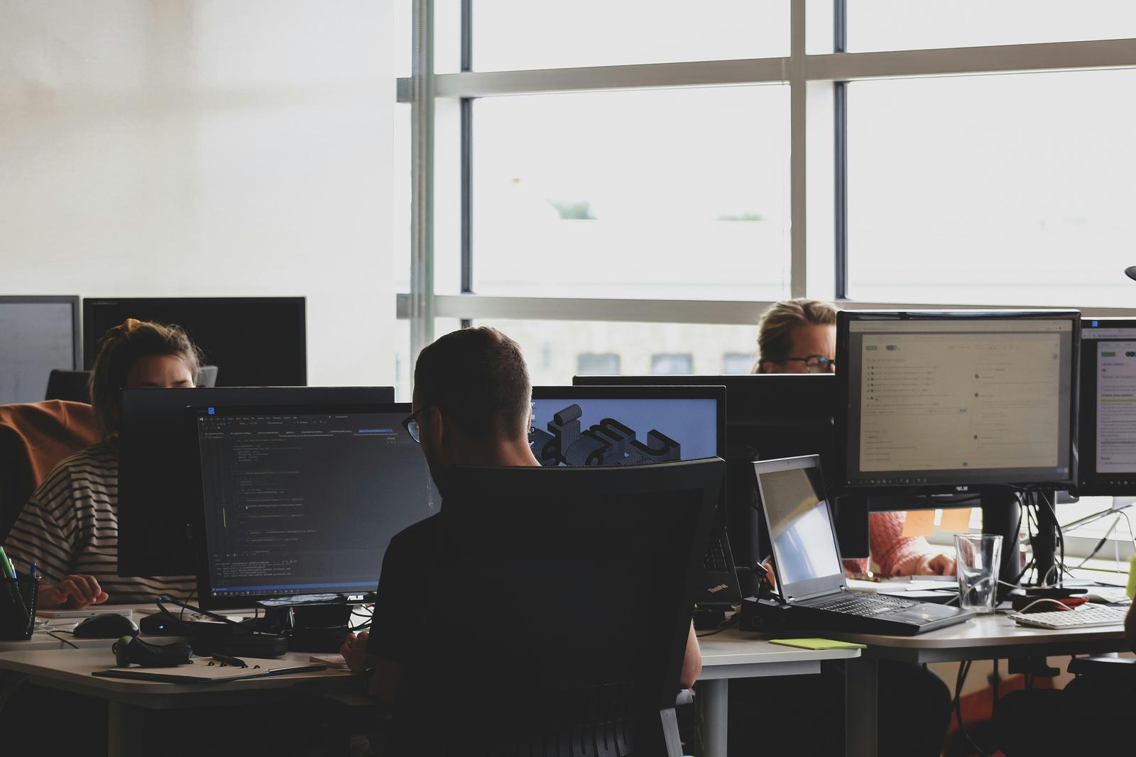Personas trabajando frente a varios monitores en una oficina